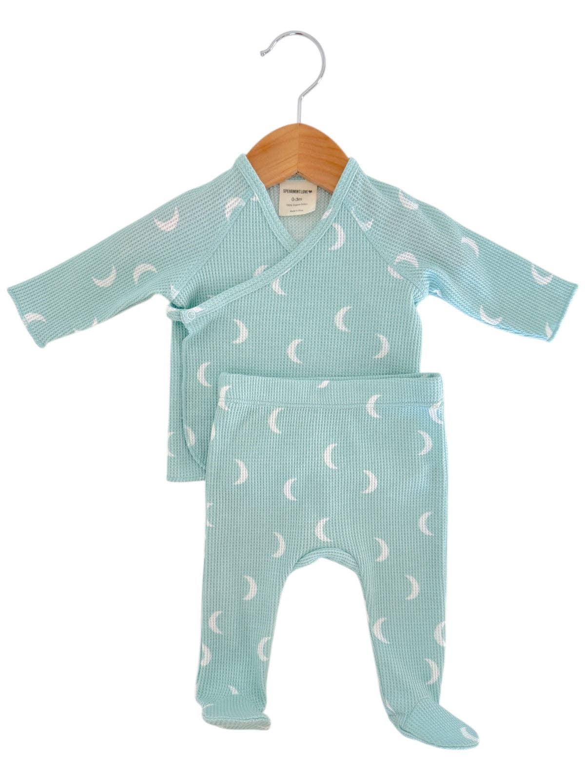 Set of baby rompers with moon pattern on a hanger against a white background