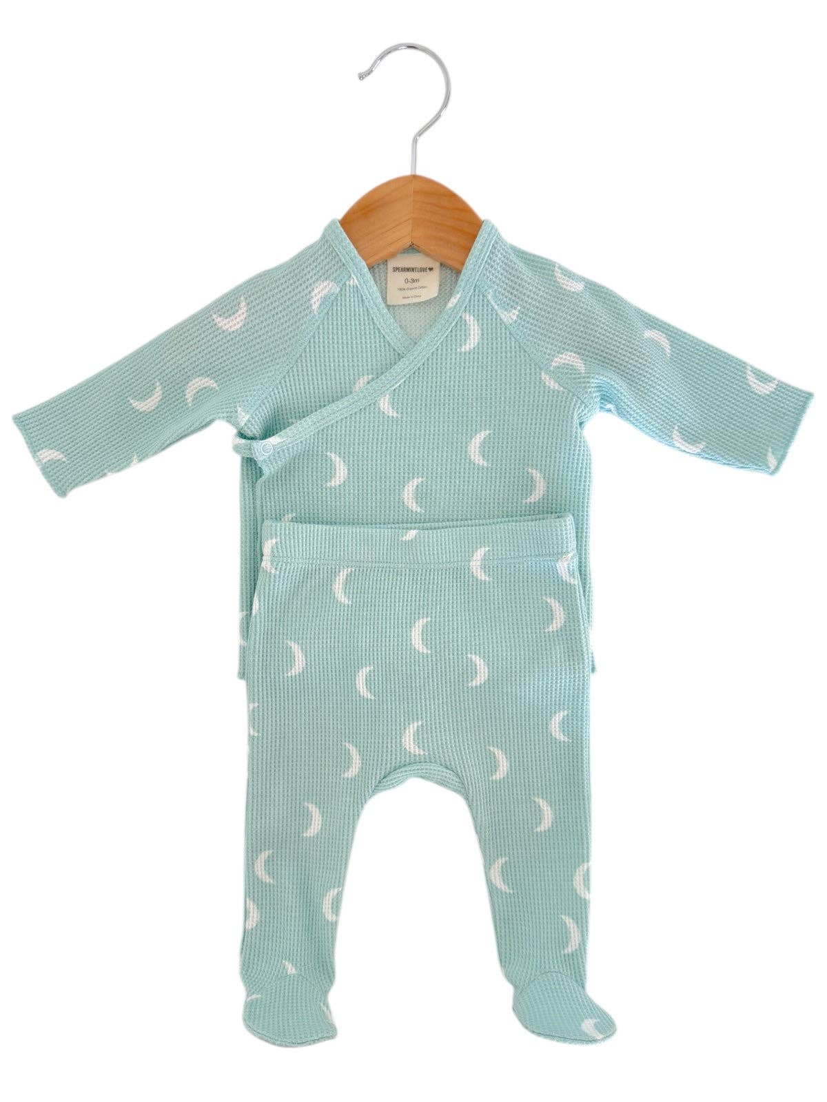 Green baby onesie with moon pattern on a hanger against a white background