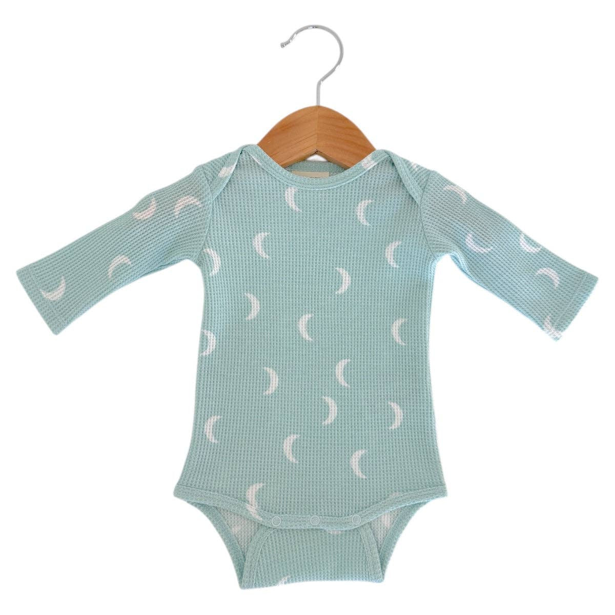 Green baby onesie with white moon pattern on a hanger against a white background