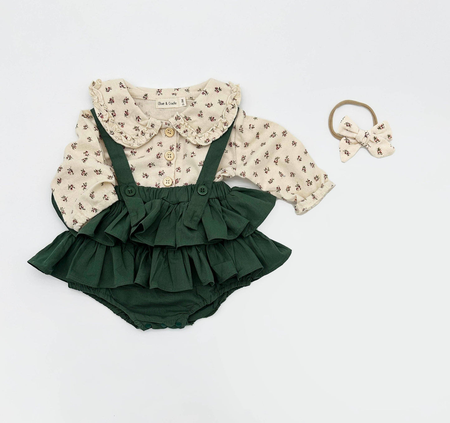 Green ruffled romper with floral blouse and hair bow on a white background