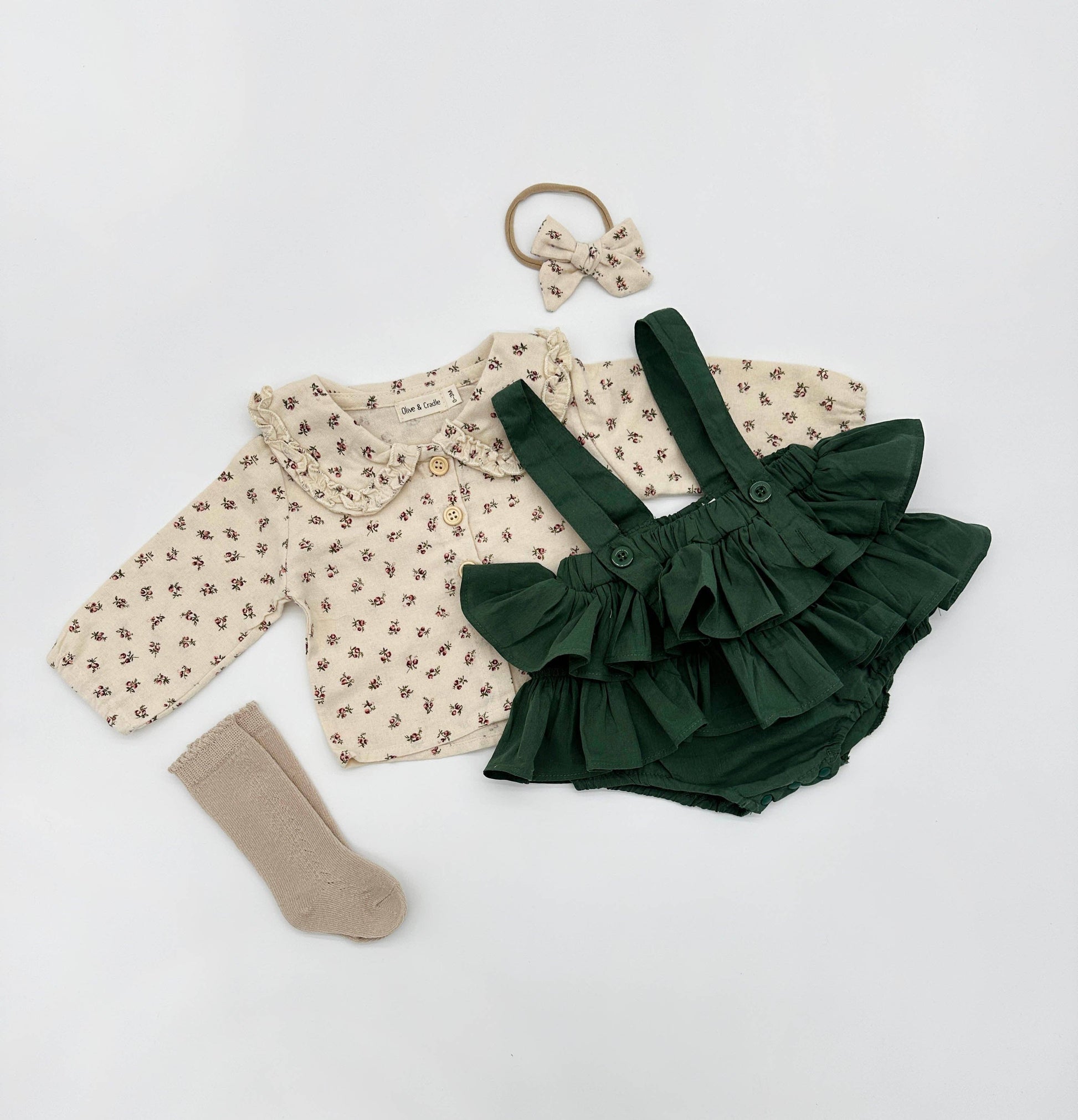 Baby outfit set with floral cardigan, green ruffled romper, beige socks, and hair clip on a white background
