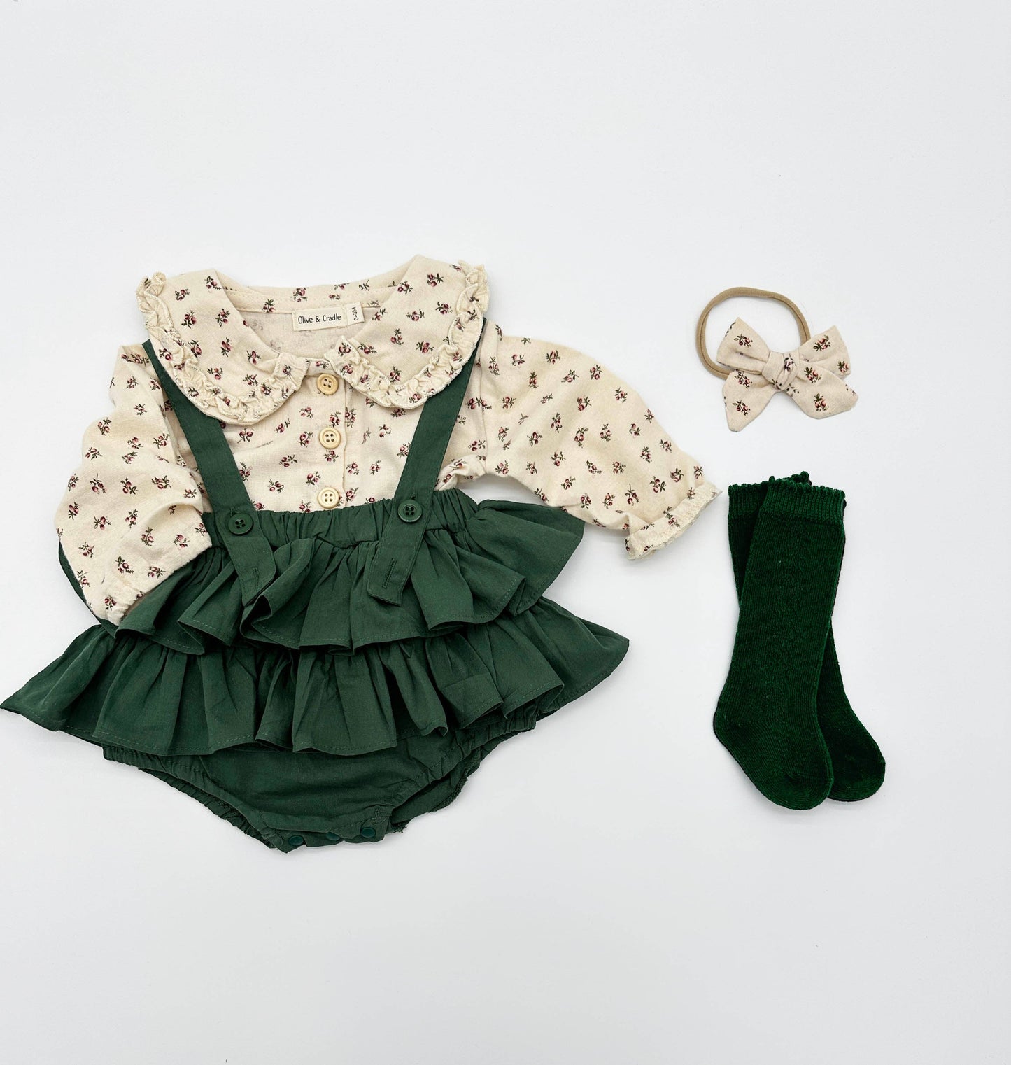 Green ruffled outfit with floral blouse, green socks, and hair accessory on a light gray background