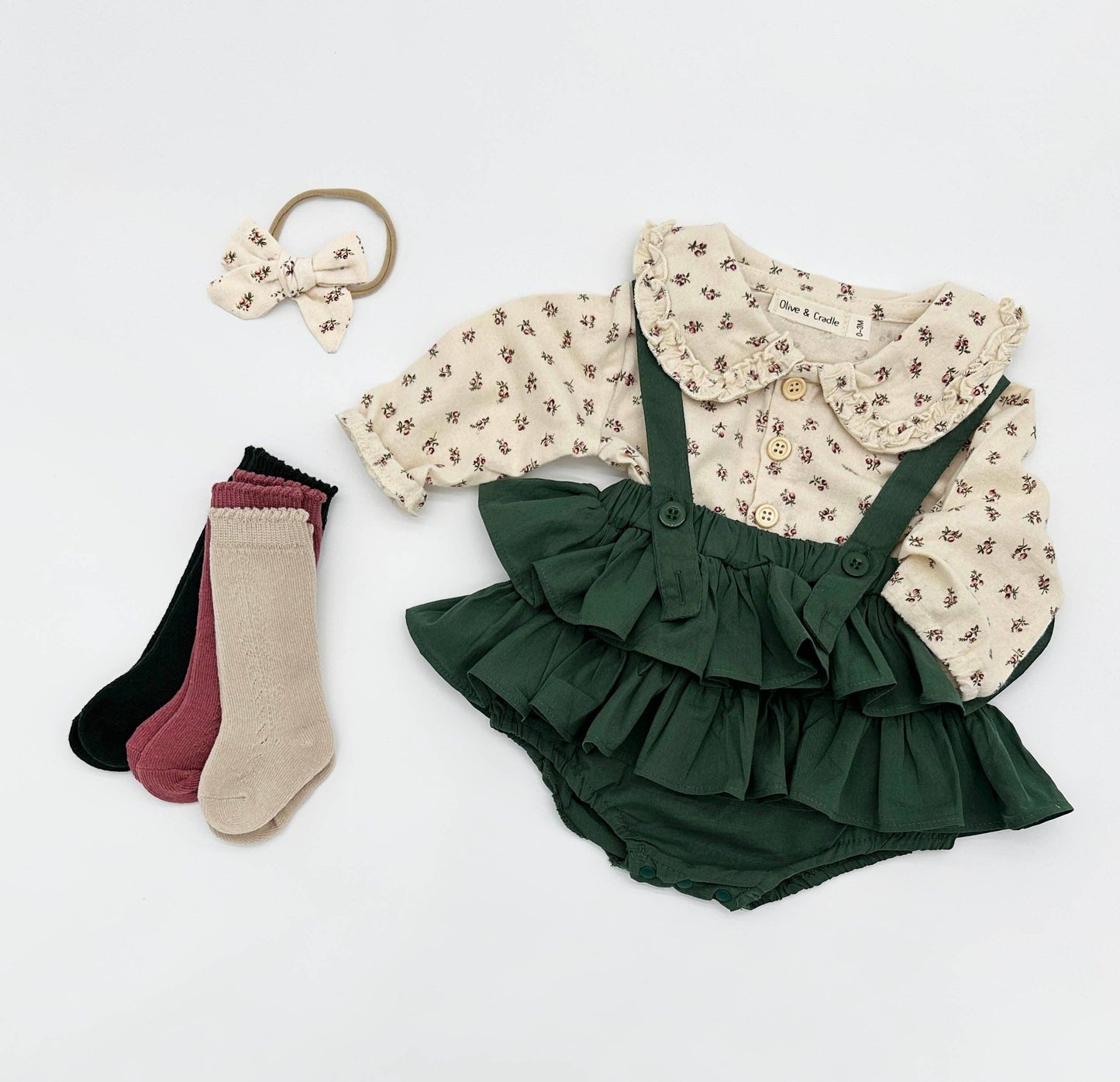 Baby outfit with floral shirt, green ruffled bloomers, and socks on a white background
