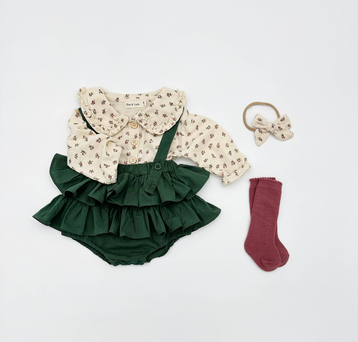Baby outfit set with green ruffled bloomers, floral top, socks, and hair tie on a white background