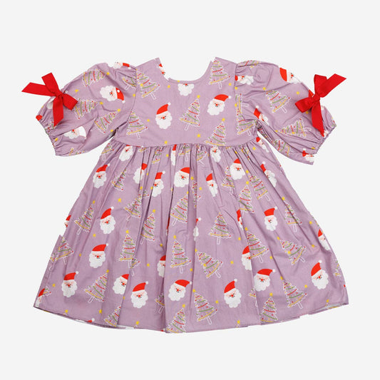 A baby girl's long-sleeve dress in dusty lavender purple, featuring an all-over print of Santa Claus faces and Christmas trees, with red ribbon bows on the sleeves, shown against a plain light gray background.