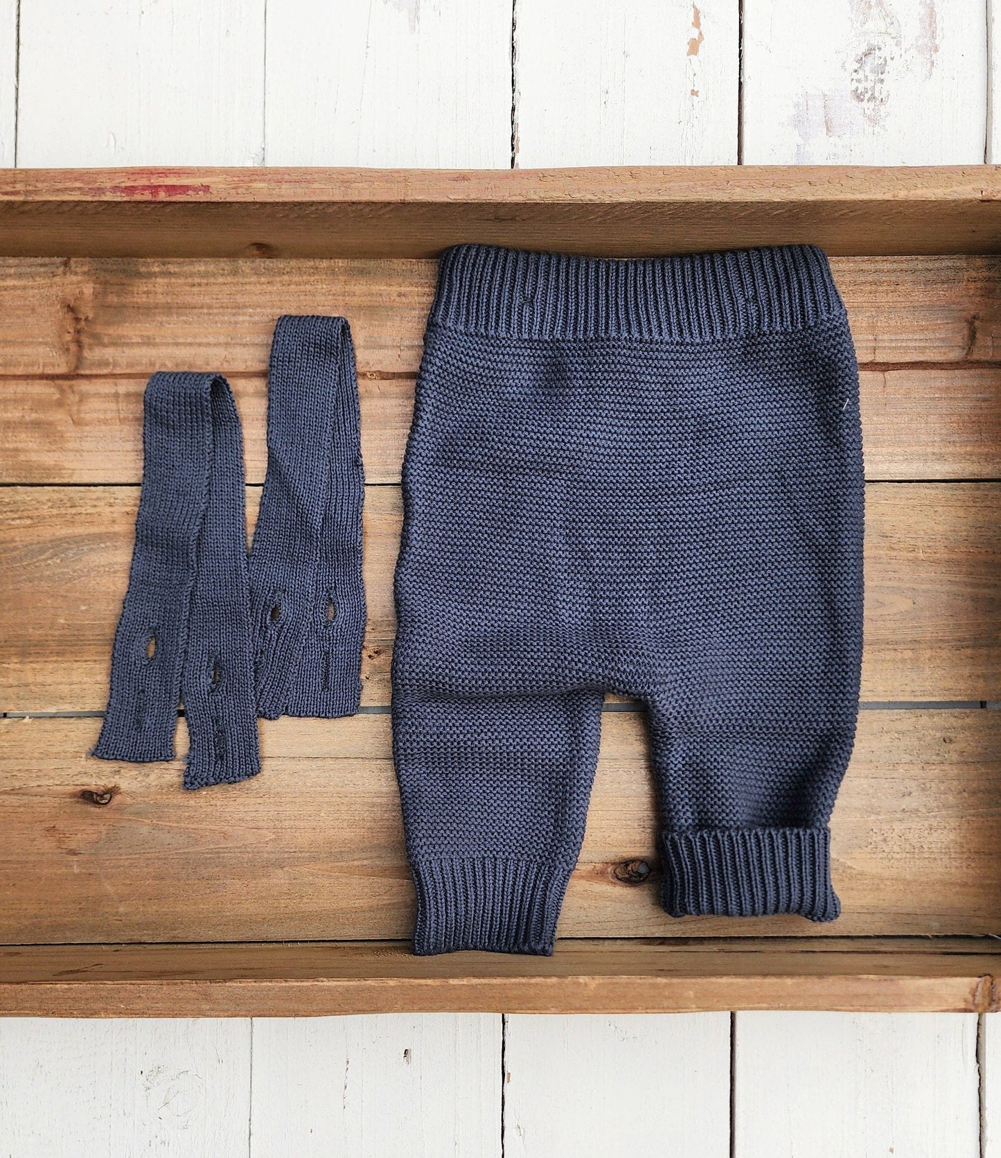 Blue knitted baby pants and booties on a wooden surface