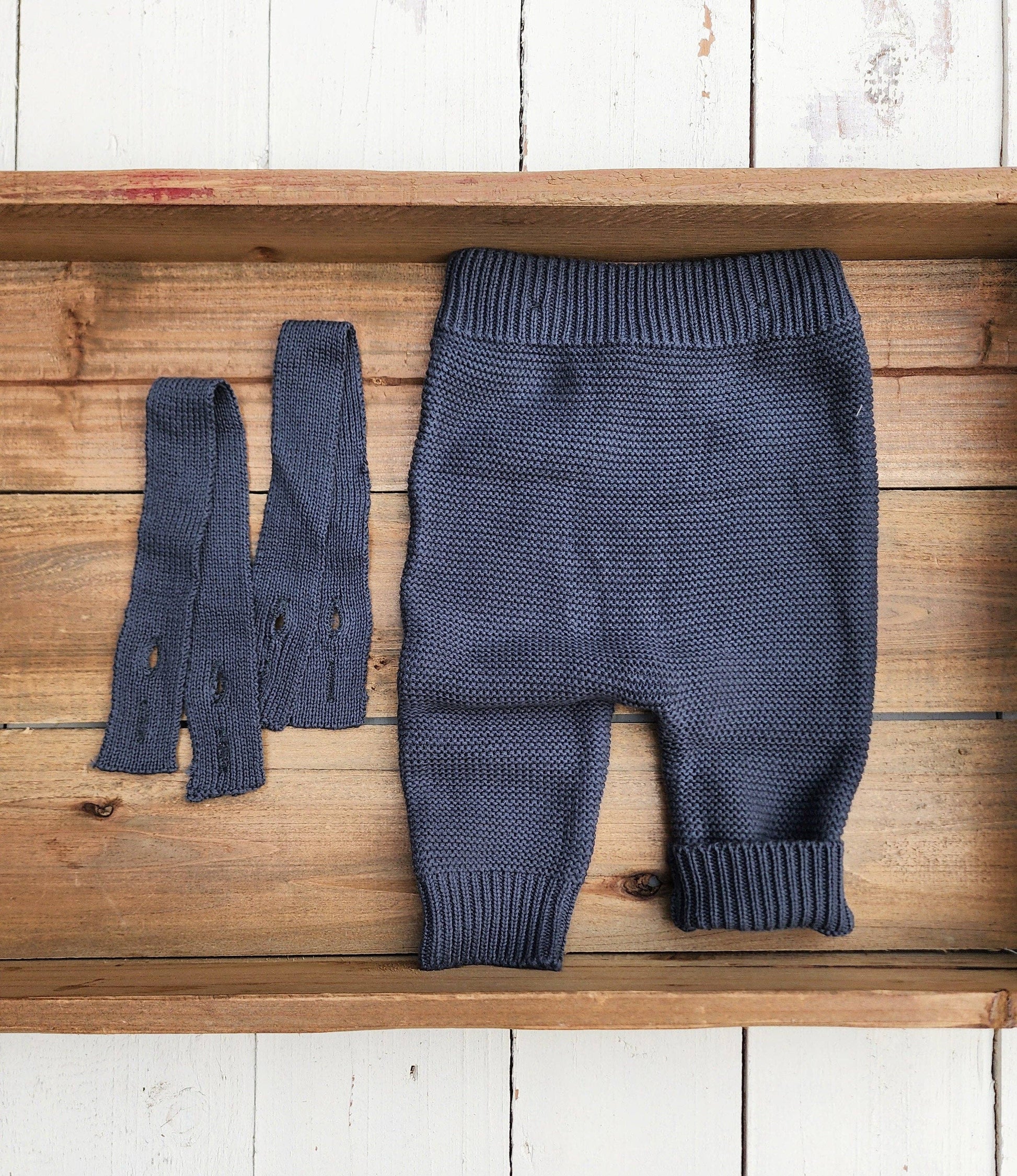 Blue knitted baby pants and booties on a wooden surface