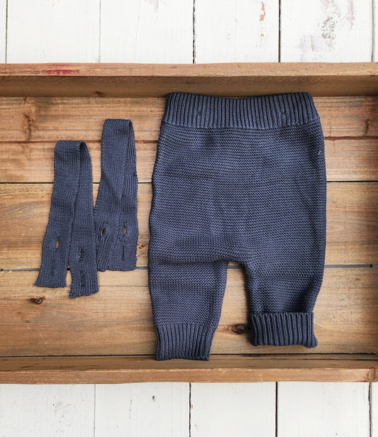 Blue knitted baby pants and booties on a wooden surface
