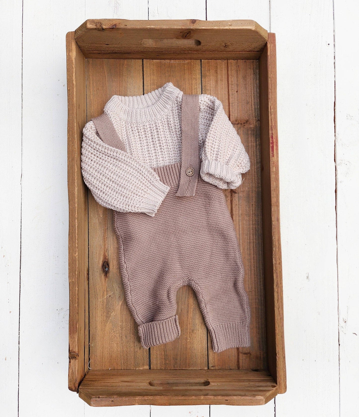 Knitted baby outfit with sweater and overalls on a wooden tray