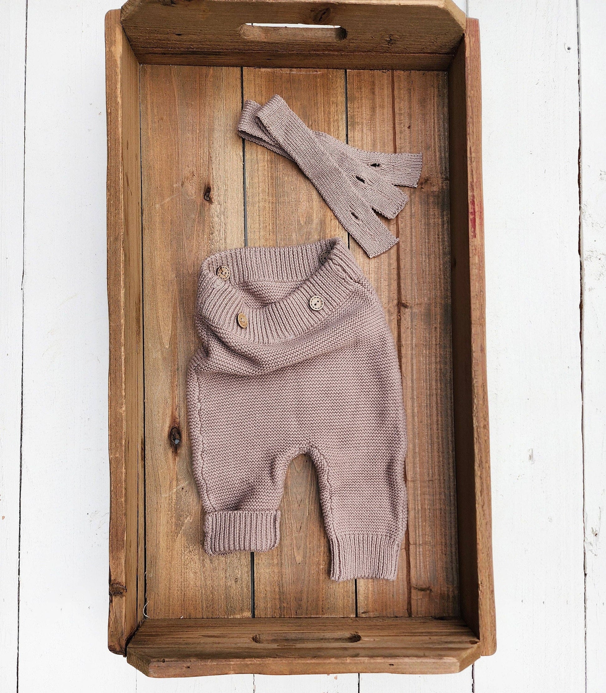 Knitted baby outfit with pants and hat on a wooden tray