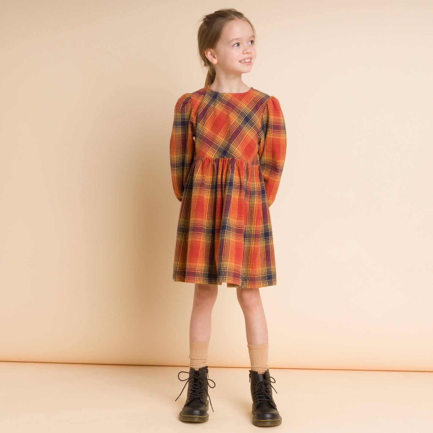 Young girl wearing a plaid dress standing against a beige background