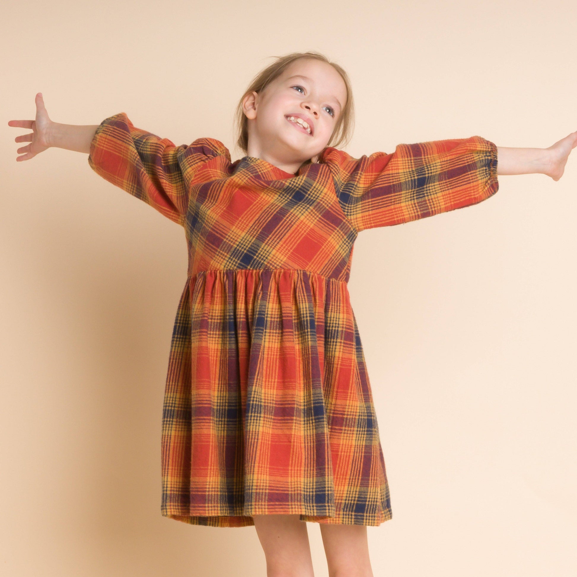 Child wearing a plaid dress with arms outstretched on a beige background