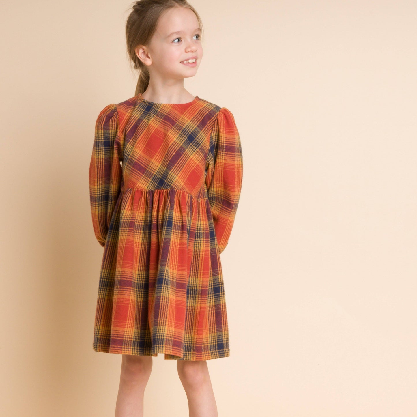 Young girl wearing a plaid dress on a beige background
