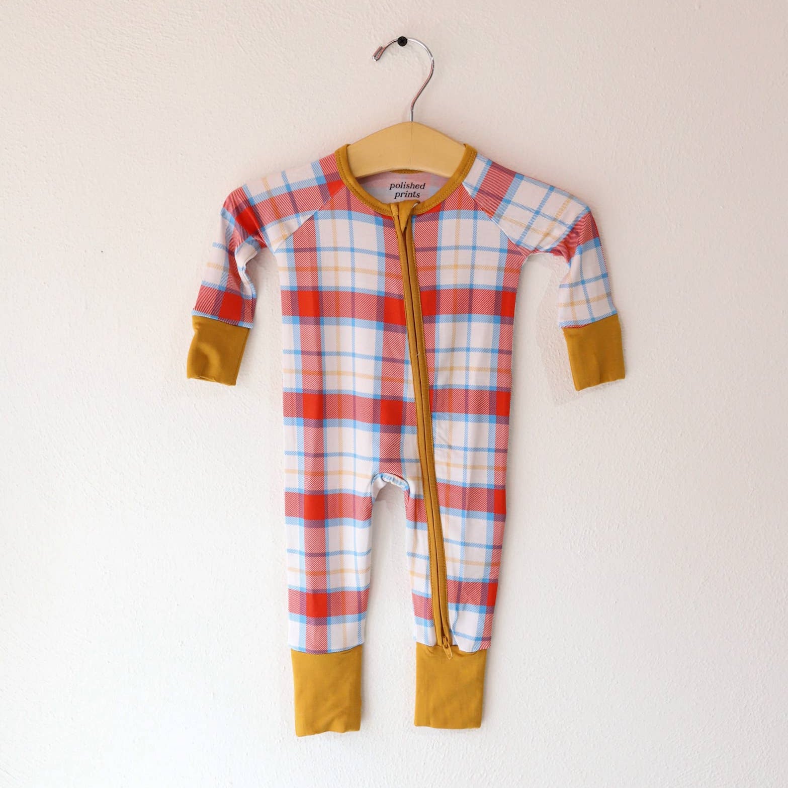 Plaid baby onesie with yellow cuffs and hem on a hanger against a white background