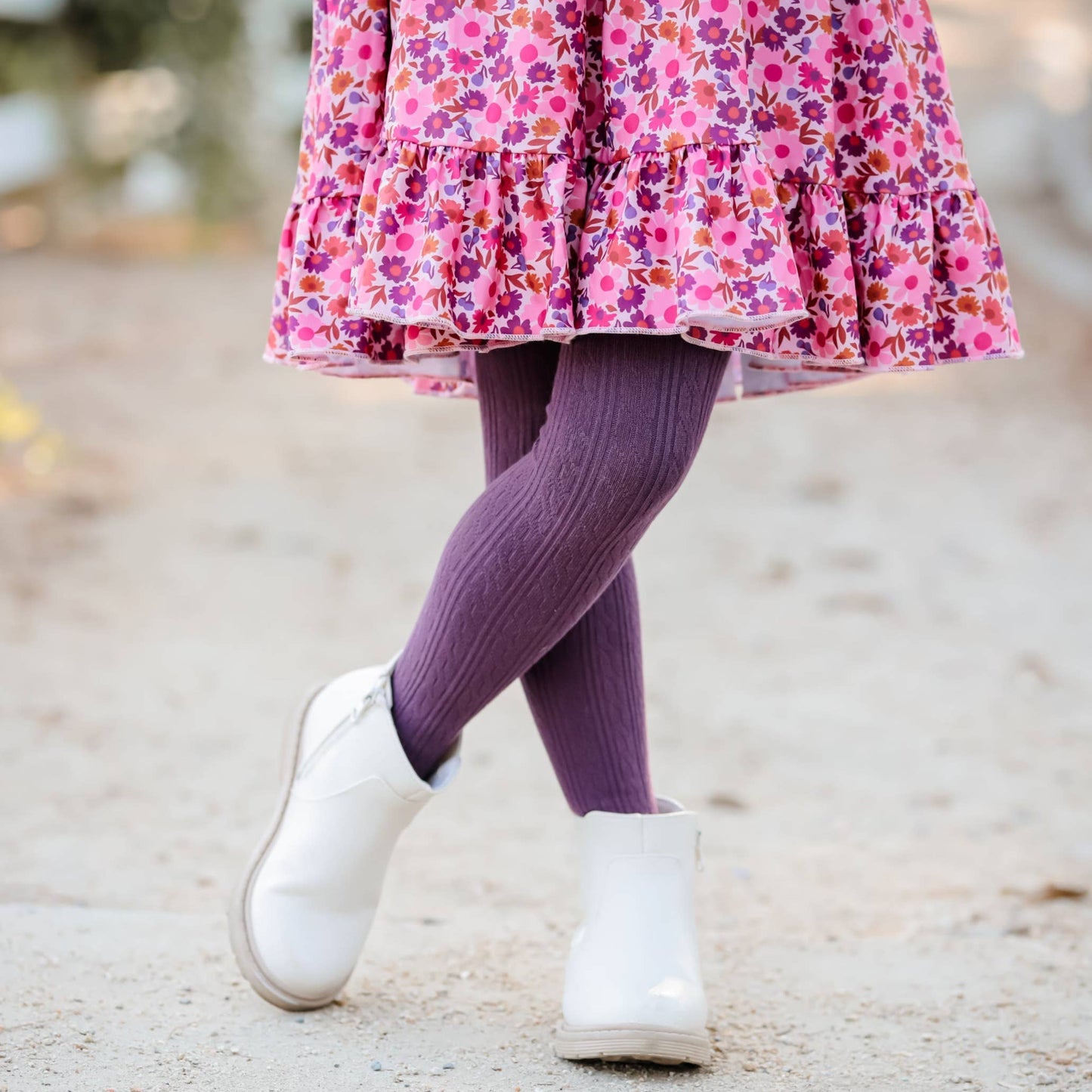 Child wearing a pink floral dress, purple tights, and white boots on a natural background