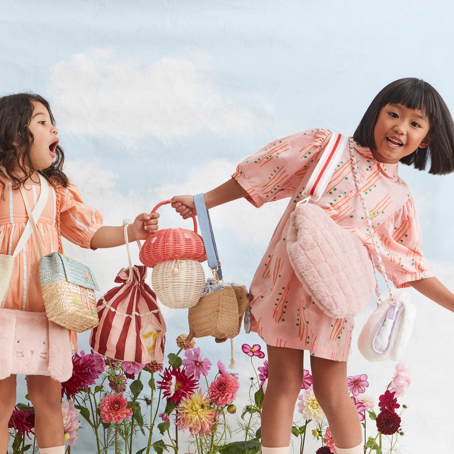 Two children in pink outfits standing among flowers with a clear blue sky.