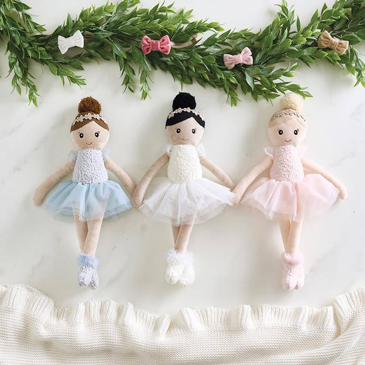 Three doll ballerinas in tutus with greenery on a white background