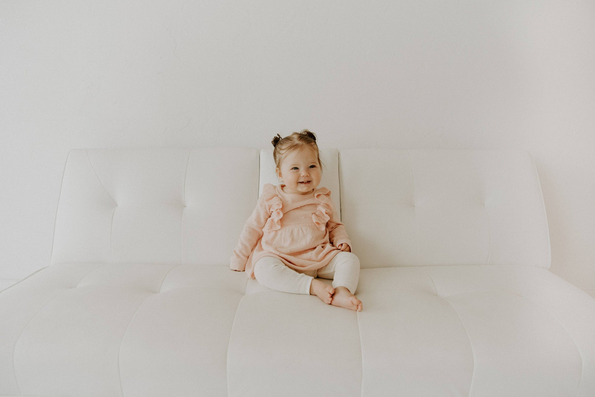 Baby sitting on a white cushion against a plain background