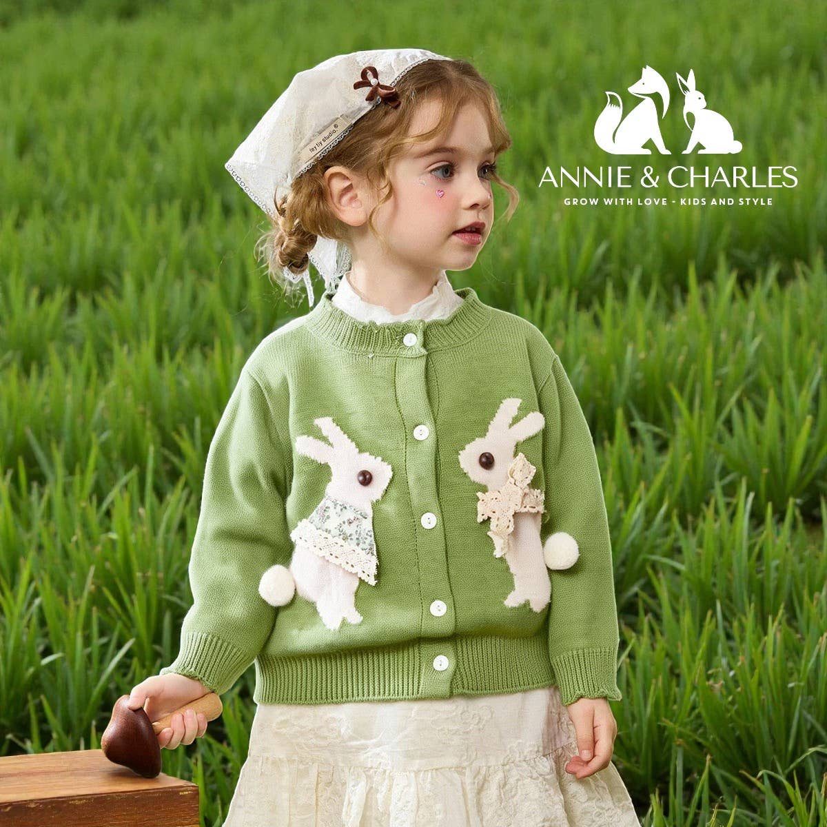 Young girl wearing a green sweater with bunny designs in a grassy field, featuring the Annie & Charles brand.