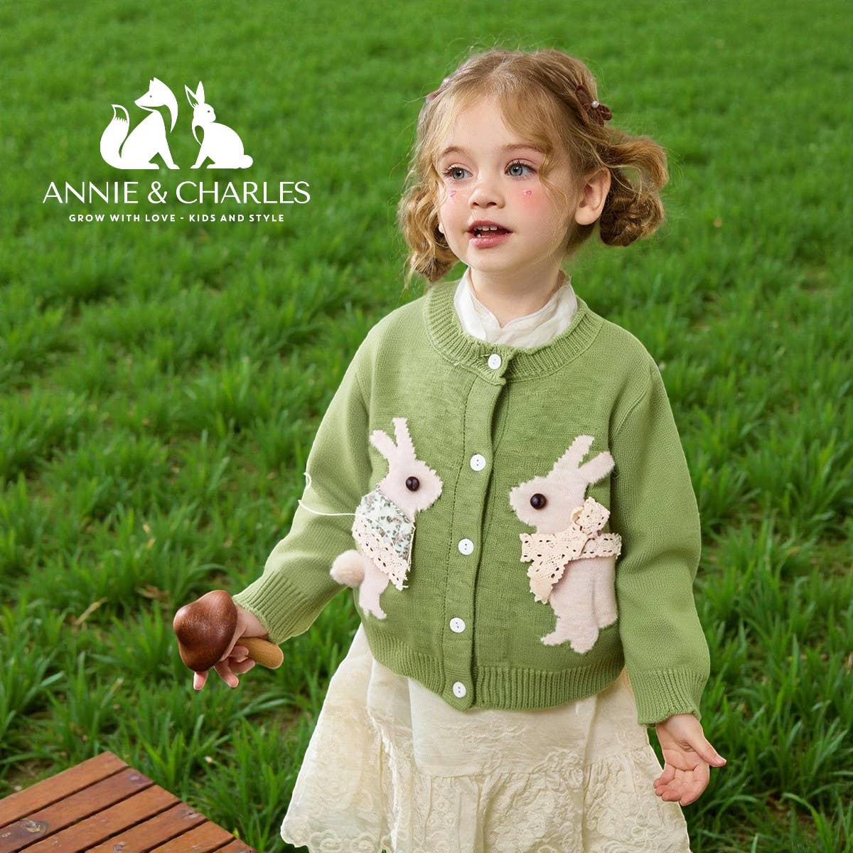 Young girl wearing a green cardigan with bunny designs outdoors, featuring the Annie & Charles brand.