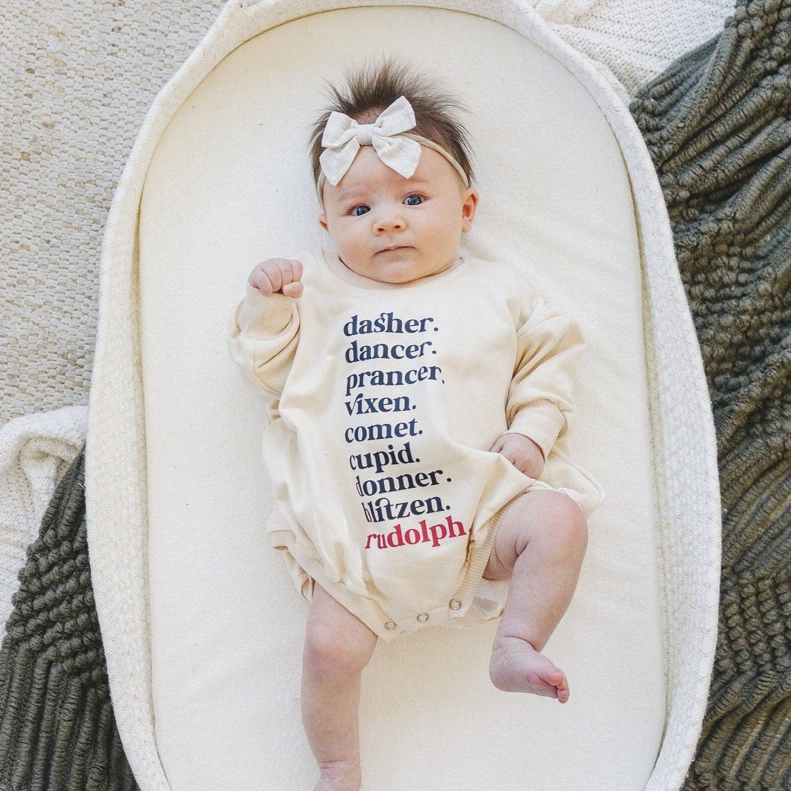 Baby in a onesie with text, lying in a white crib with a textured blanket.
