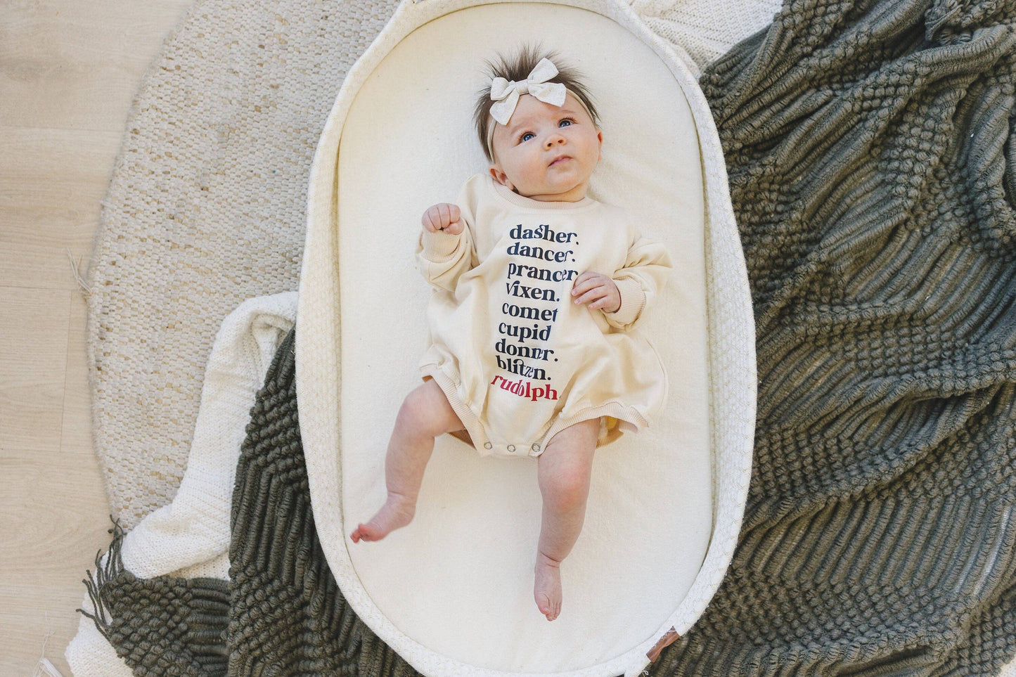 Baby in a crib with a decorative headband and text on a white blanket.