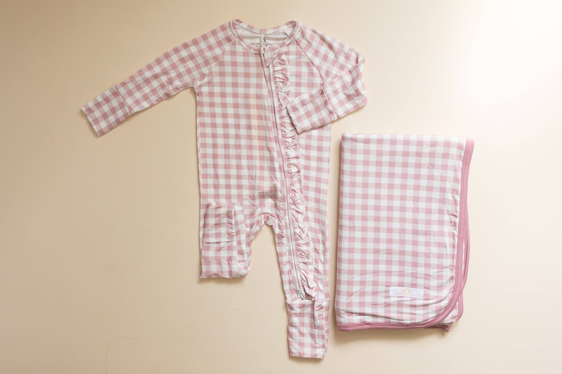 Pink gingham baby romper and blanket on a beige background