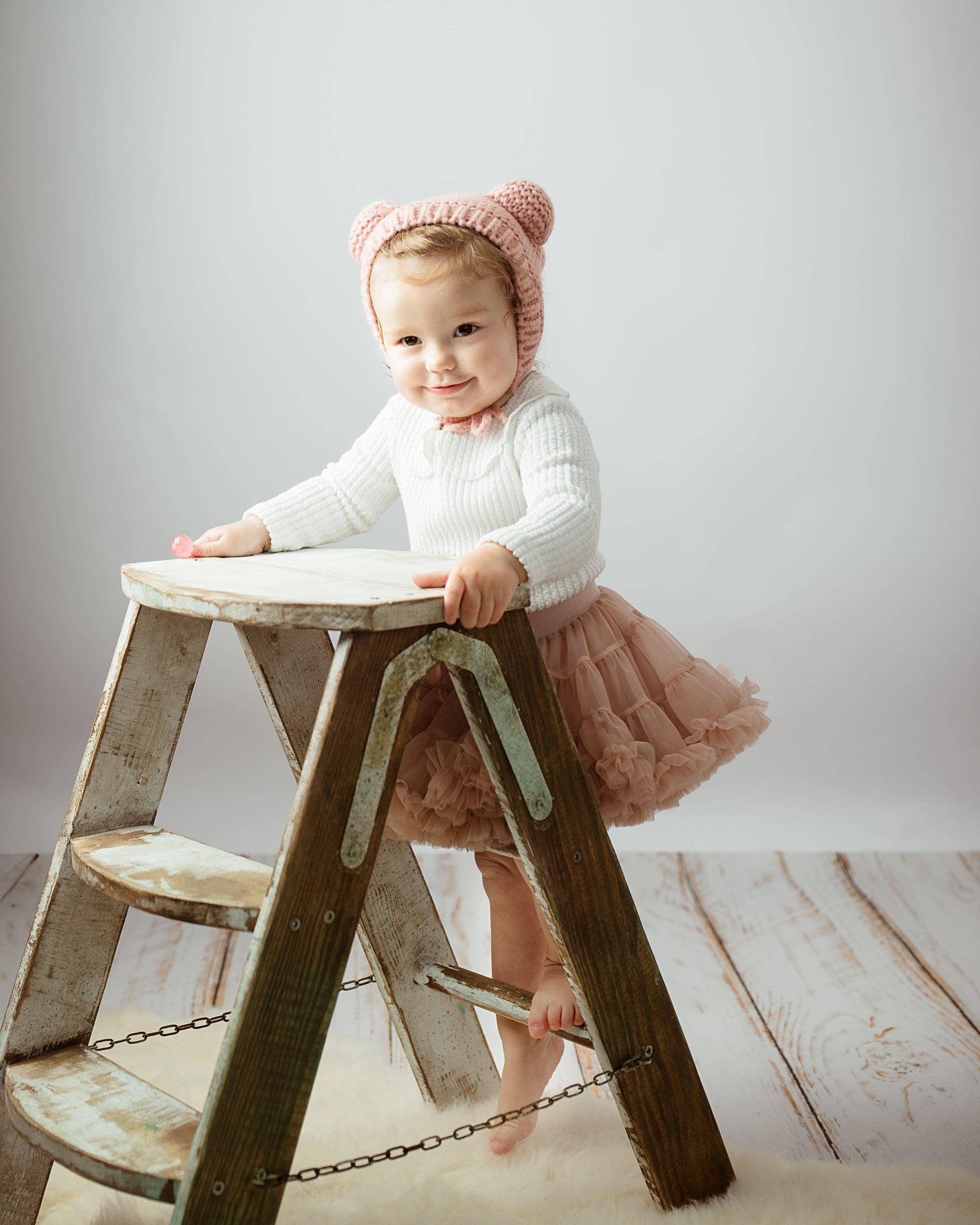 Child sitting on a wooden step stool with a plain background