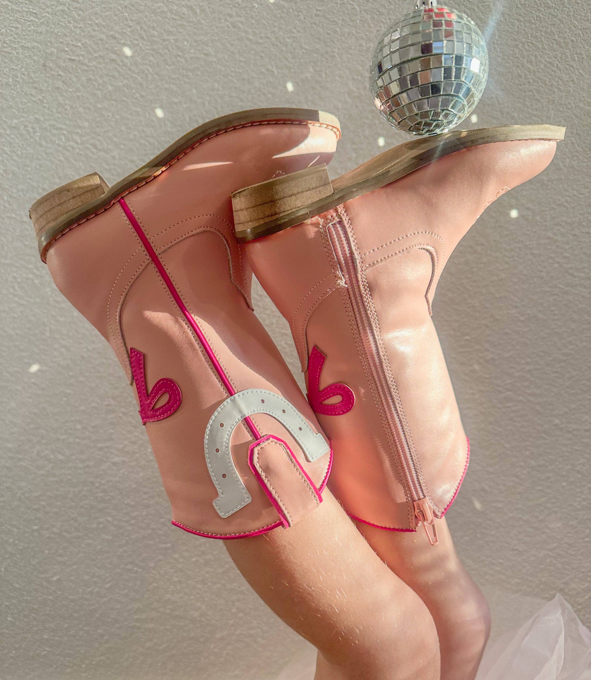 Pink cowboy boots with pink horseshoe design on a neutral background