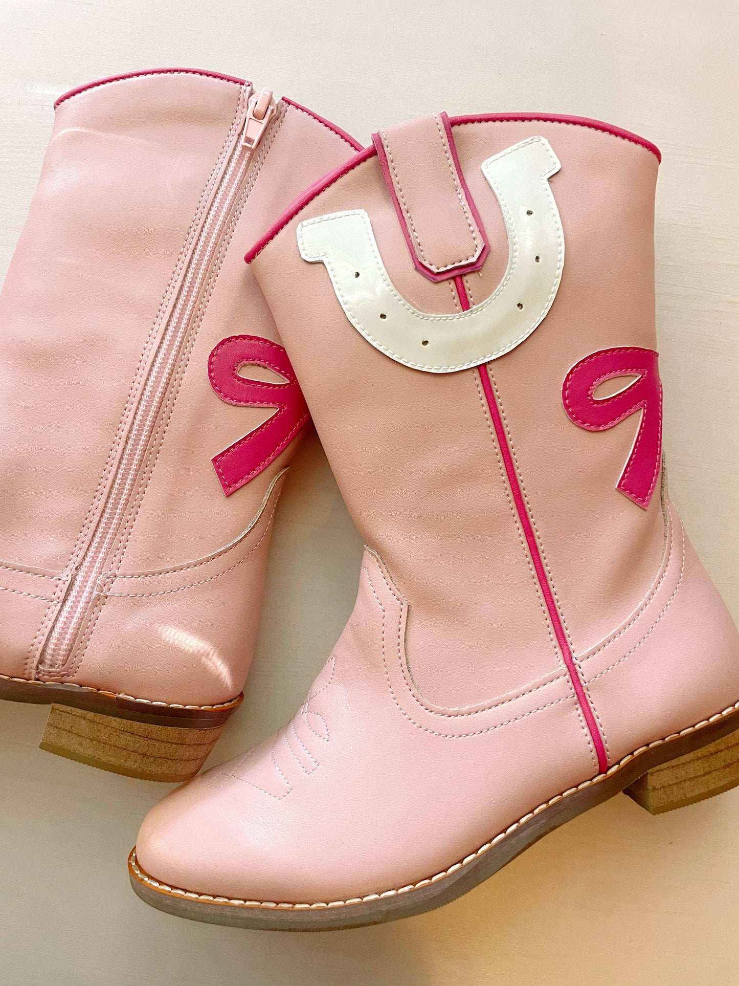 Pink cowboy boots with a horseshoe design on a light background