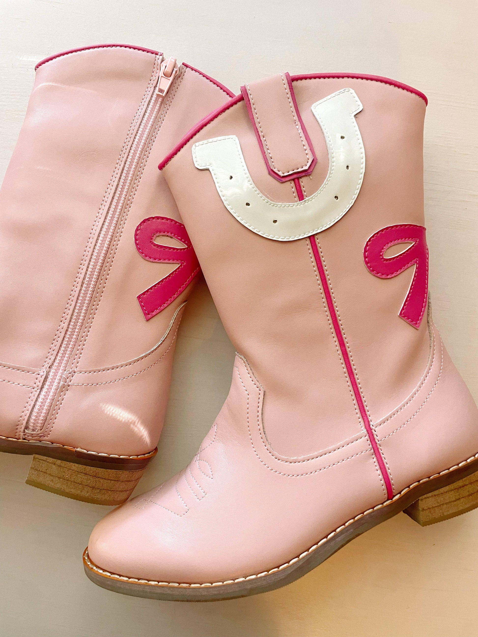 Pink cowboy boots with a horseshoe design on a light background
