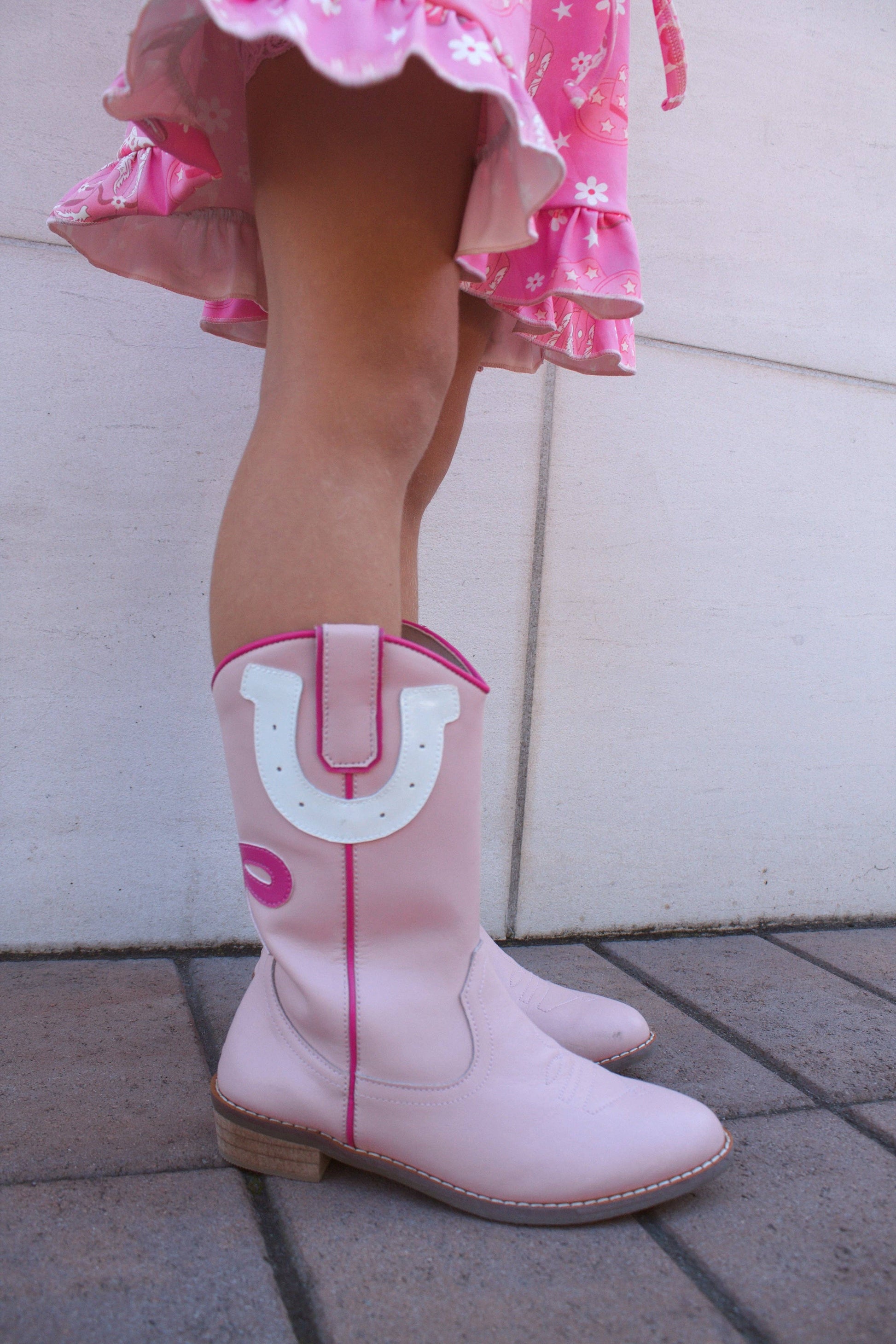 Child wearing pink cowboy boots with a large white 'U' logo on a light background