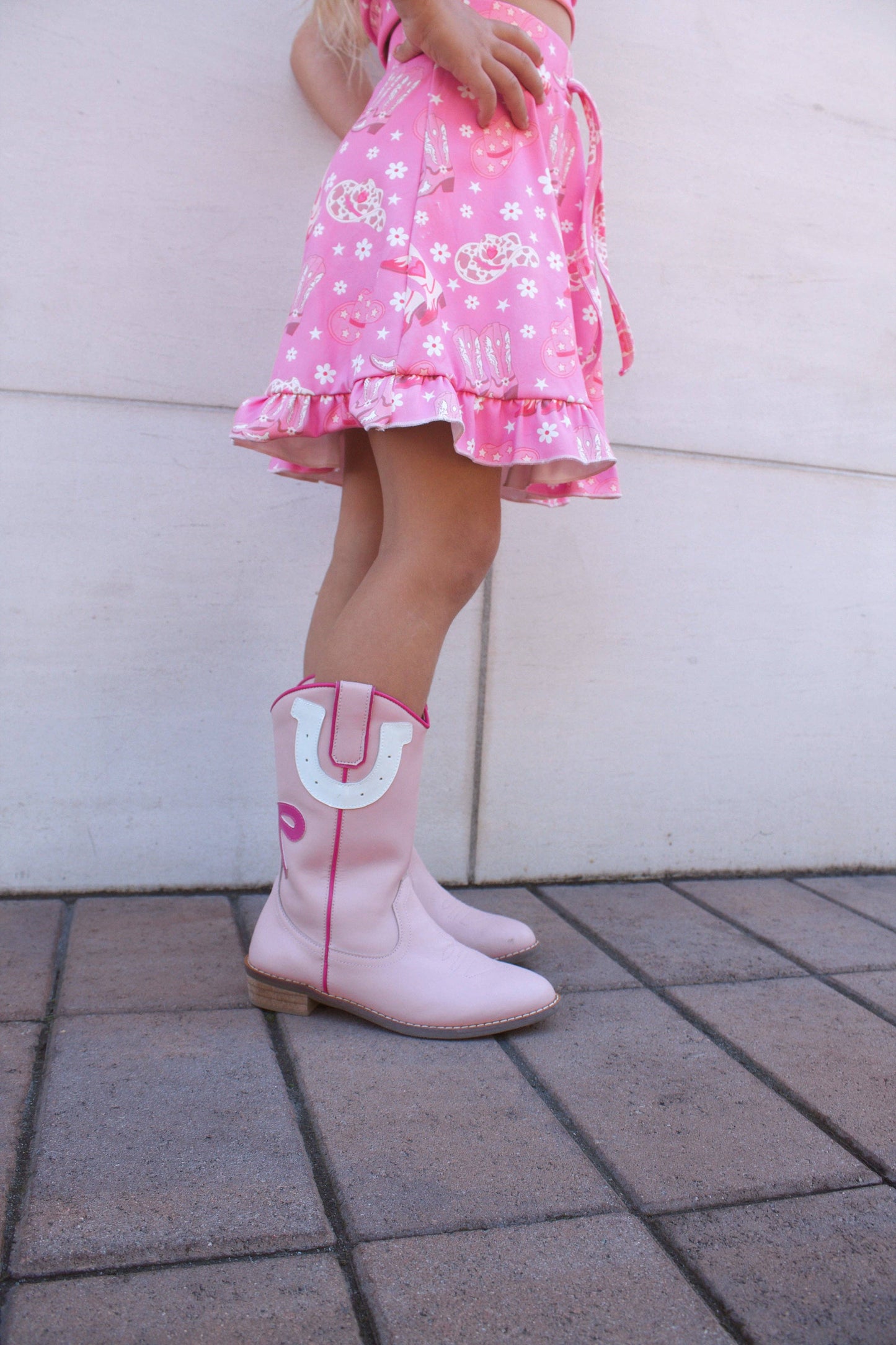 Child wearing pink dress and boots with a white background