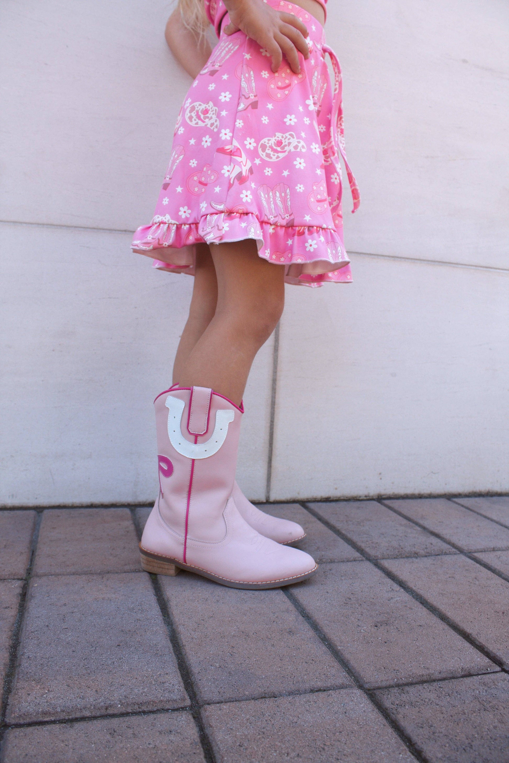 Child wearing pink dress and boots with a white background