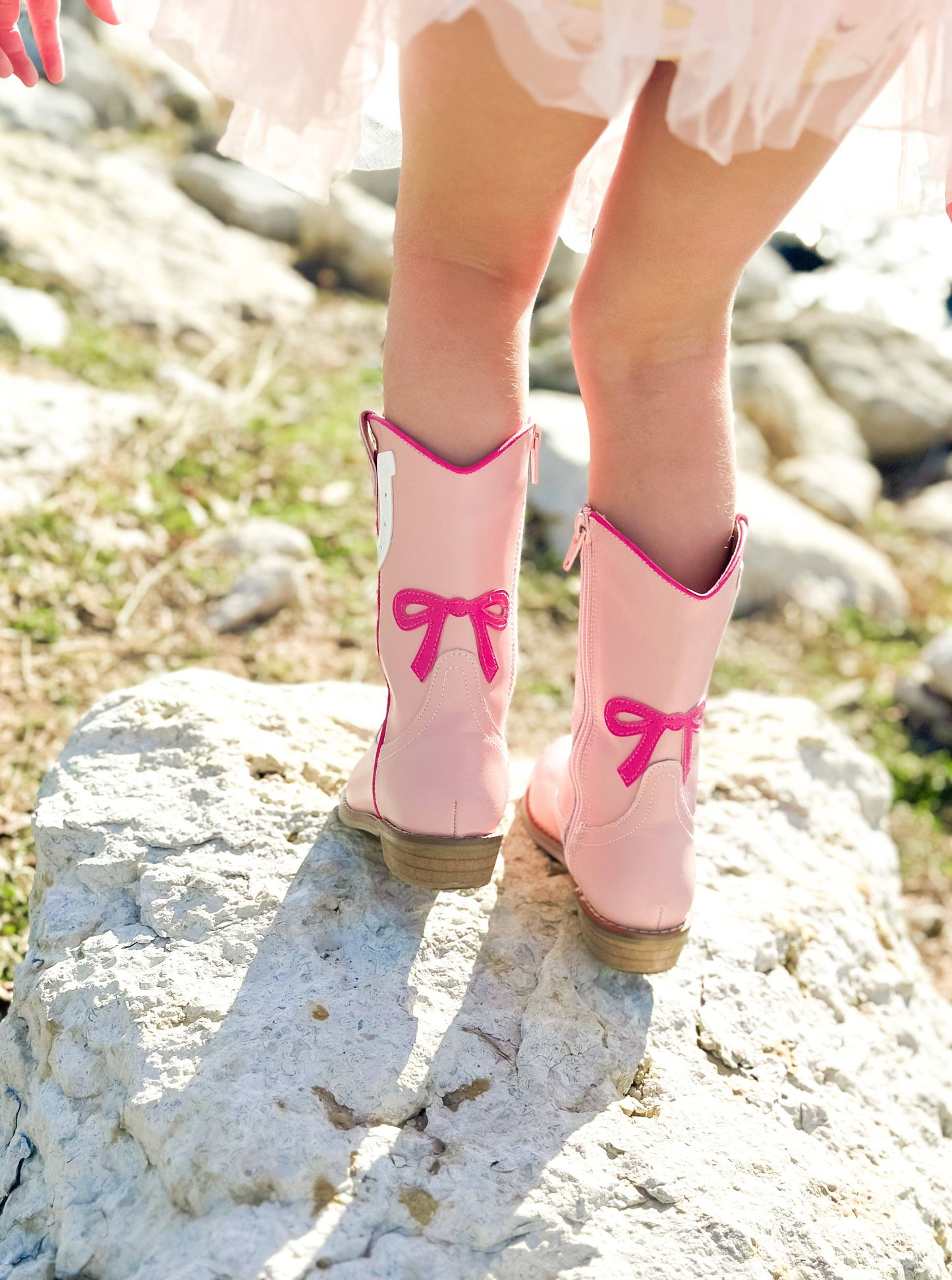 Pink cowboy boots with bows on a rocky ground