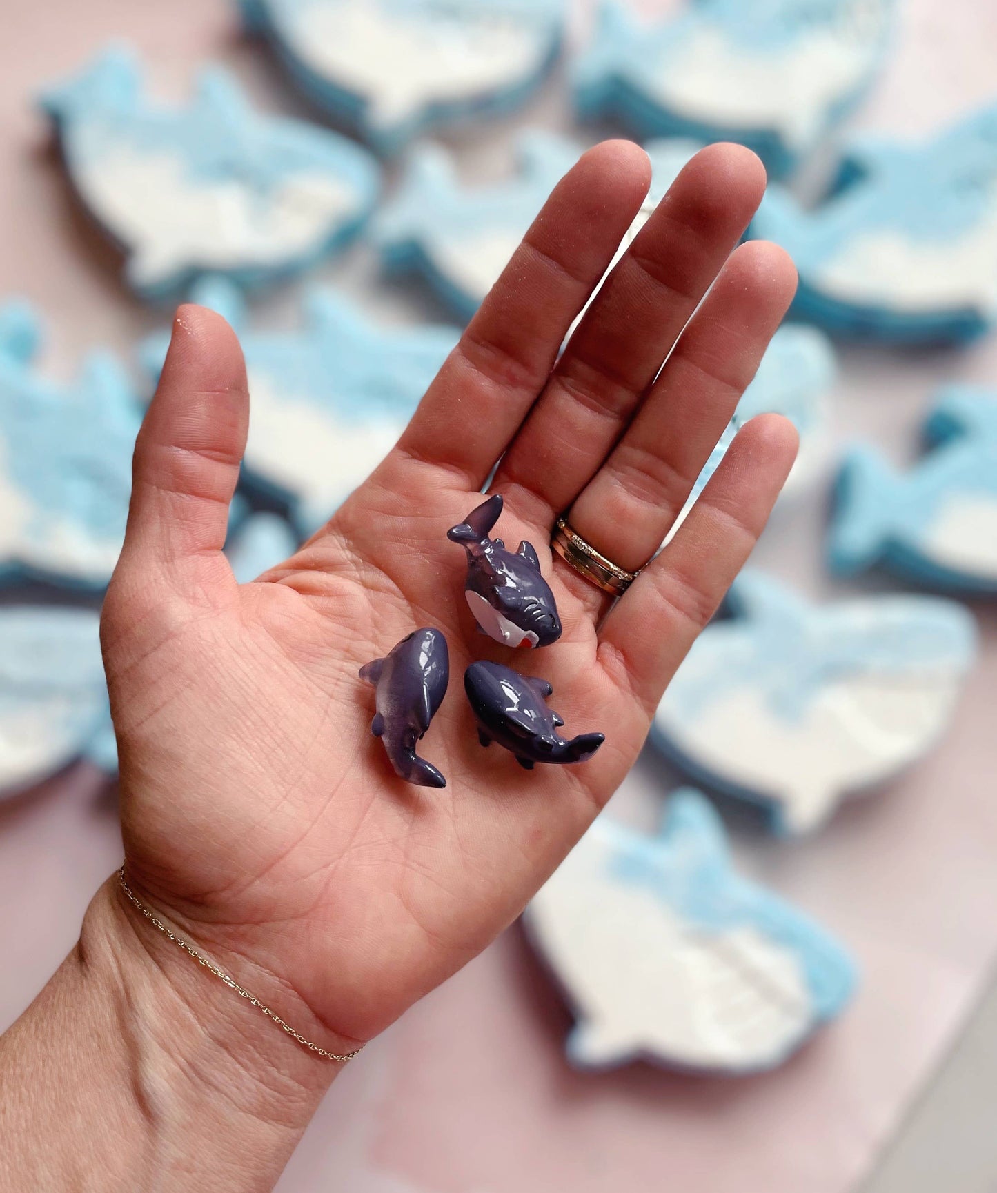 Hand holding two small purple figurines with a blurred background of similar figurines.