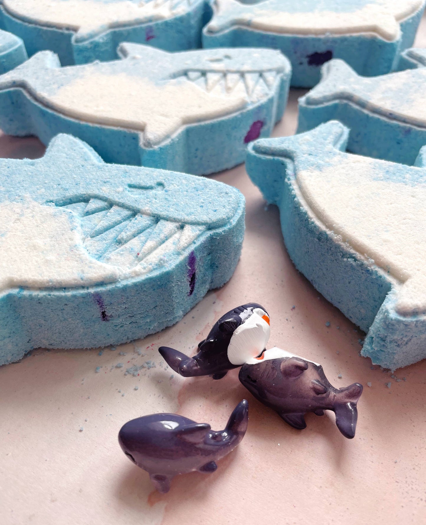 Shark-shaped bath bombs on a surface with small shark figurines.