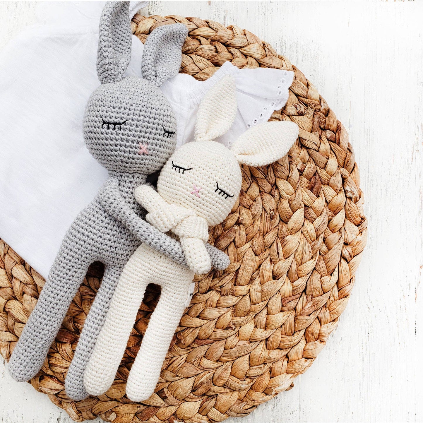 Two crocheted rabbit toys, one gray and one white, on a woven mat.