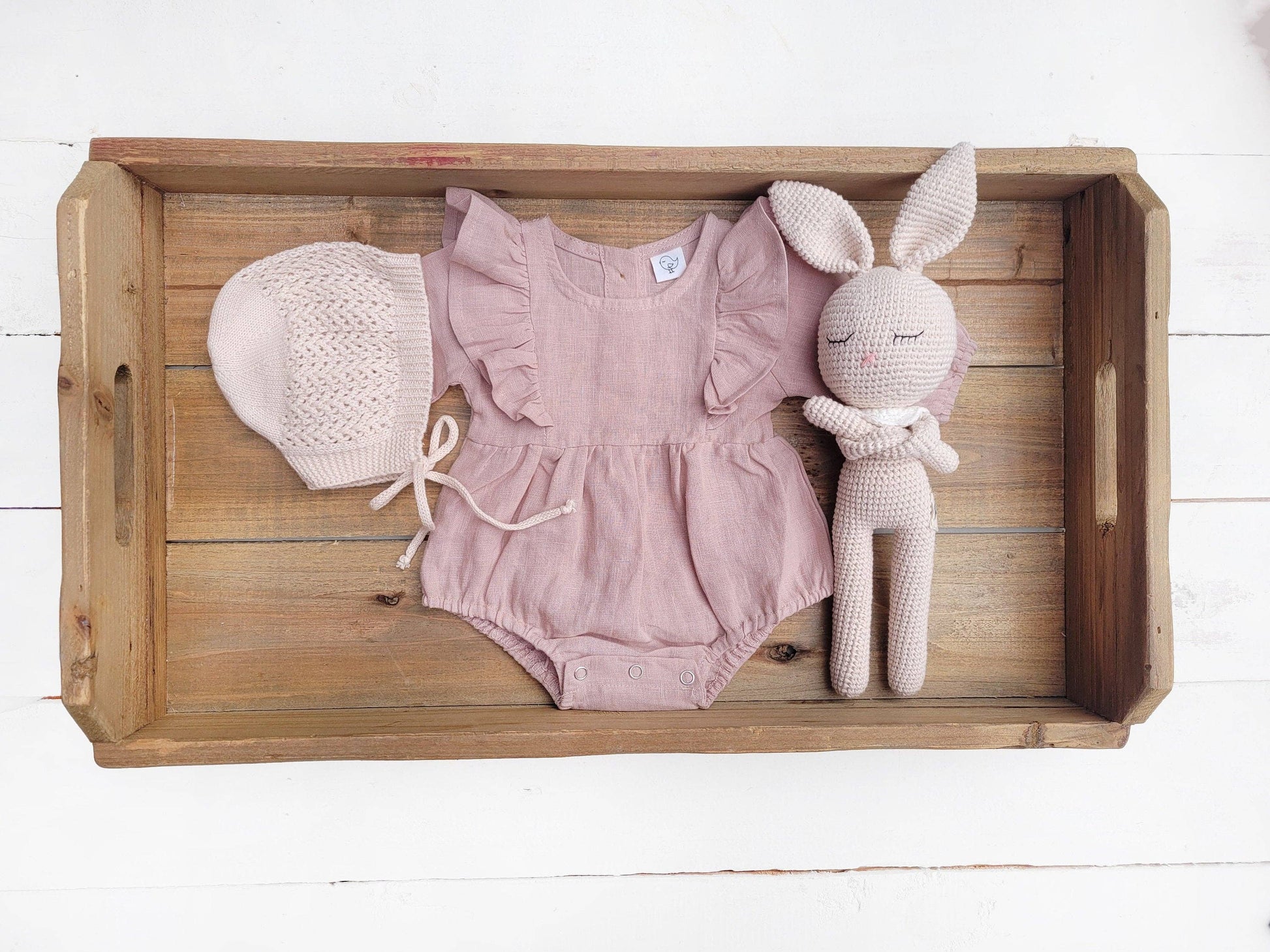 Wooden tray with baby romper, hat, and toy on a white background
