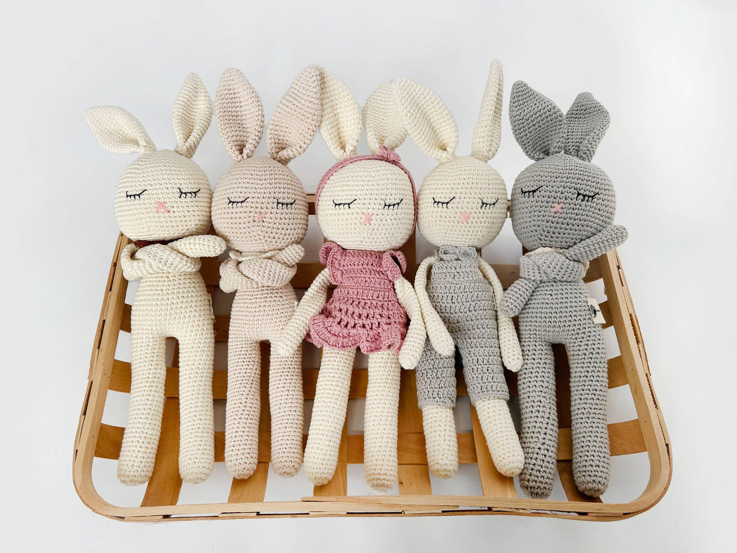 Set of five crocheted dolls with bunny ears on a wooden tray against a white background