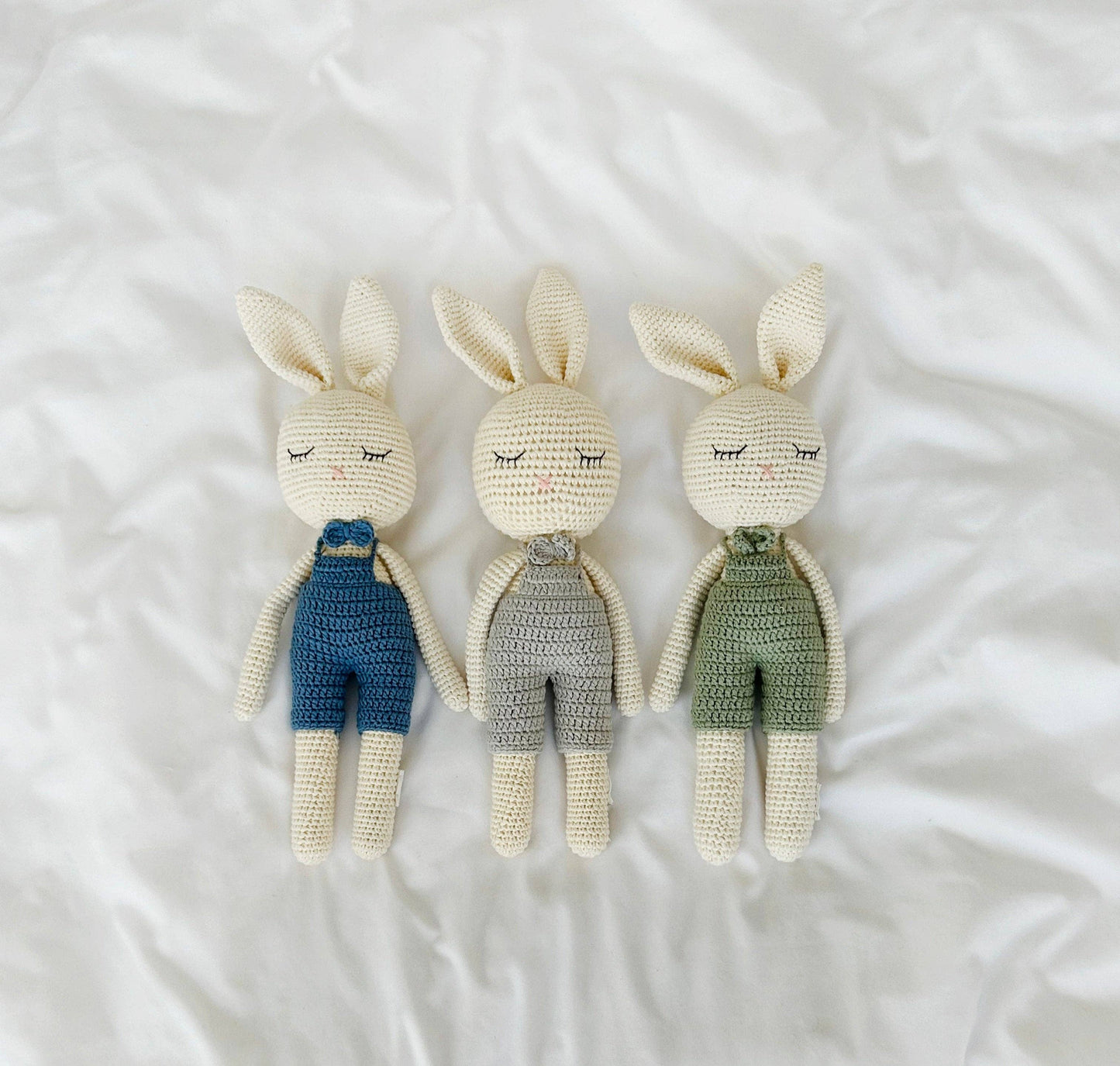 Three crocheted rabbit toys in blue, gray, and green outfits on a white background