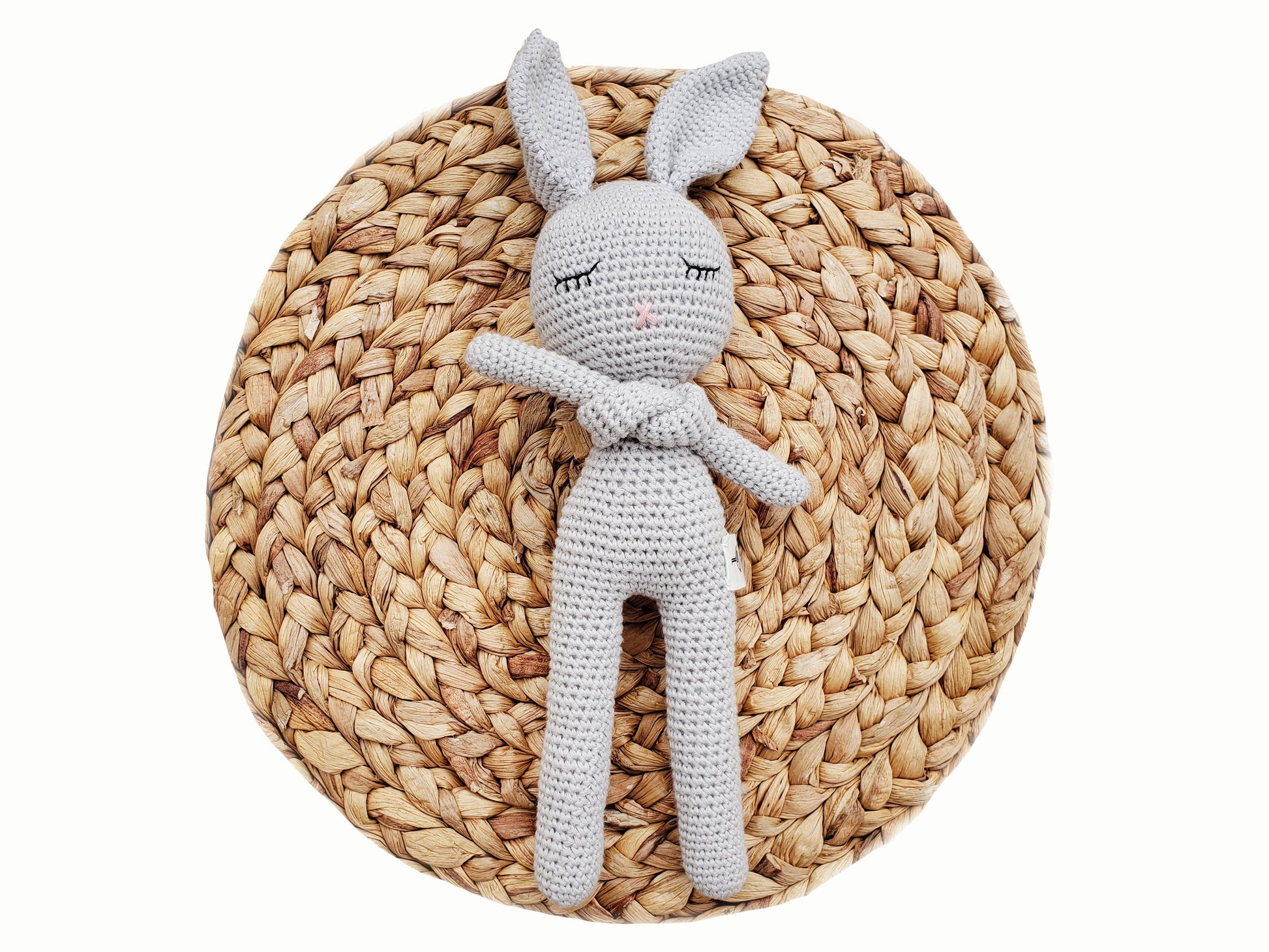 Gray crochet bunny toy on a woven mat
