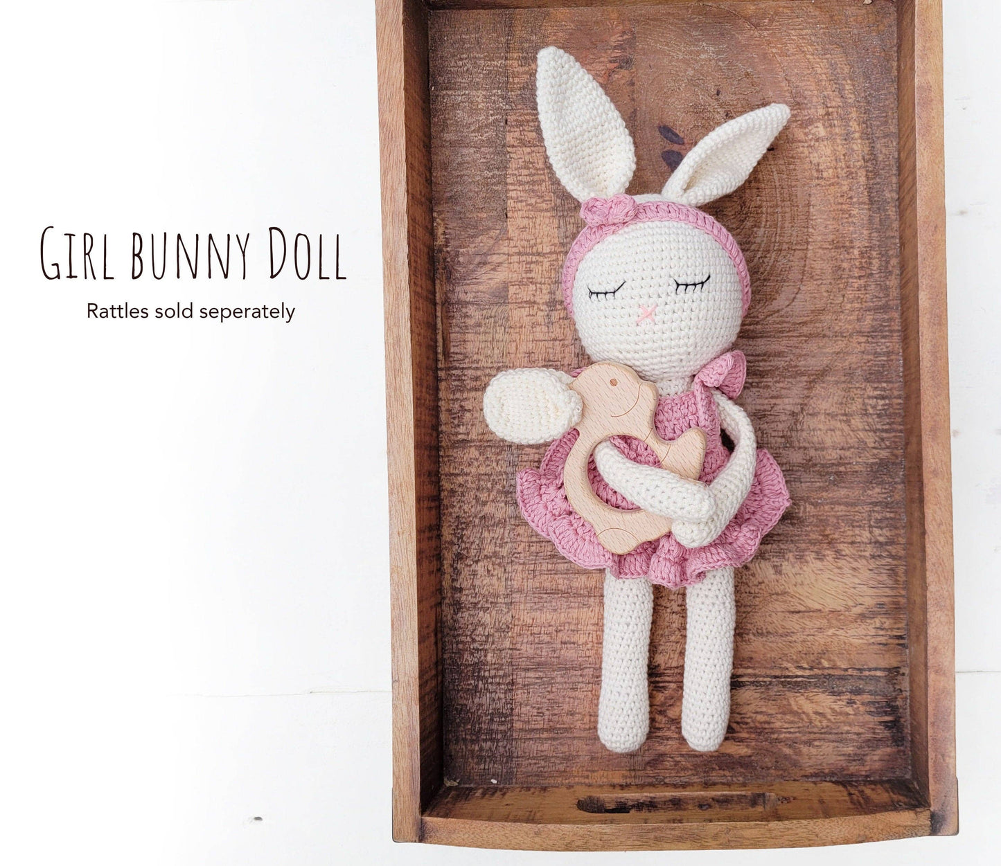 Girl bunny doll in pink outfit on a wooden tray with text about rattles sold separately.