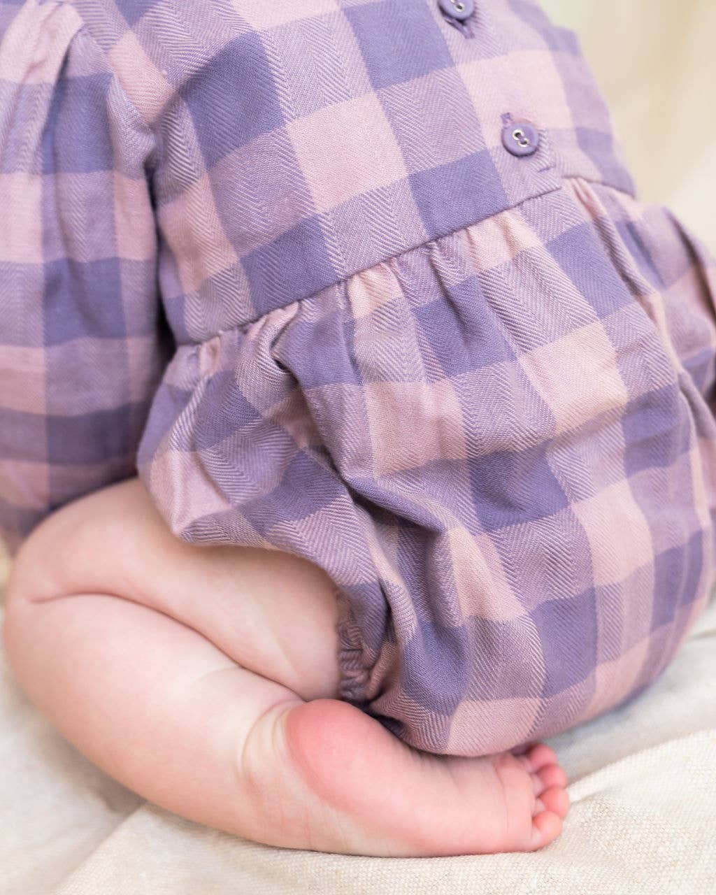 Baby wearing a purple and white checkered outfit on a light background