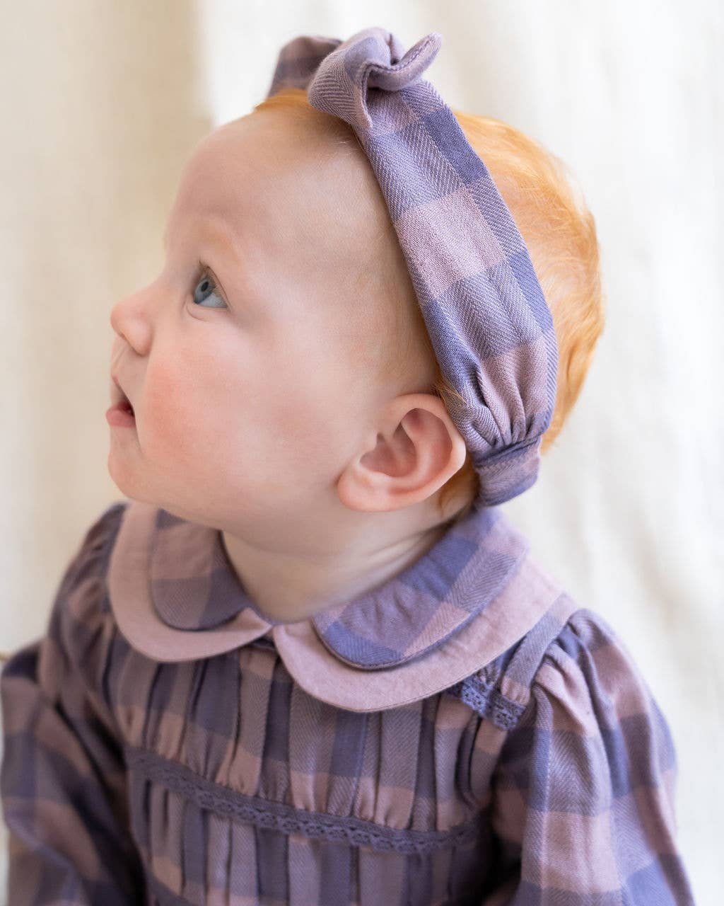 Baby wearing a plaid outfit with a matching headband against a white background