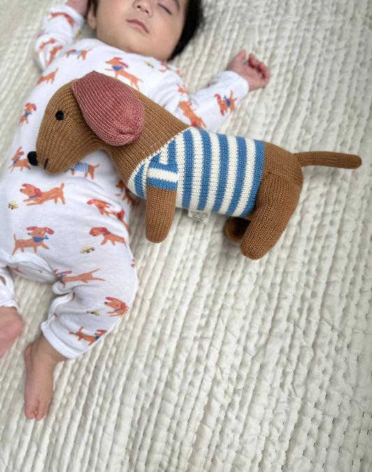 Baby lying on a textured surface with a knitted dachshund toy wearing a striped sweater.