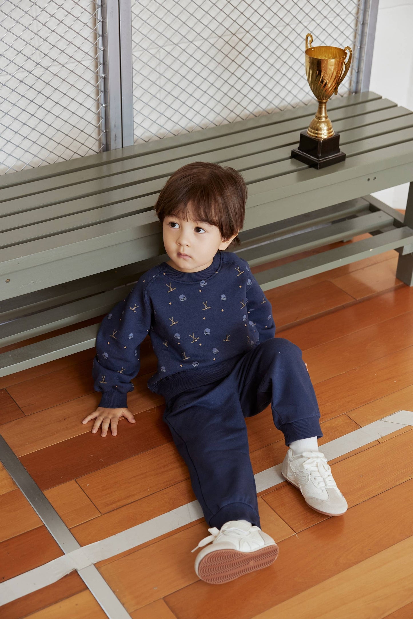 Child sitting on a wooden floor with a gold trophy in the background