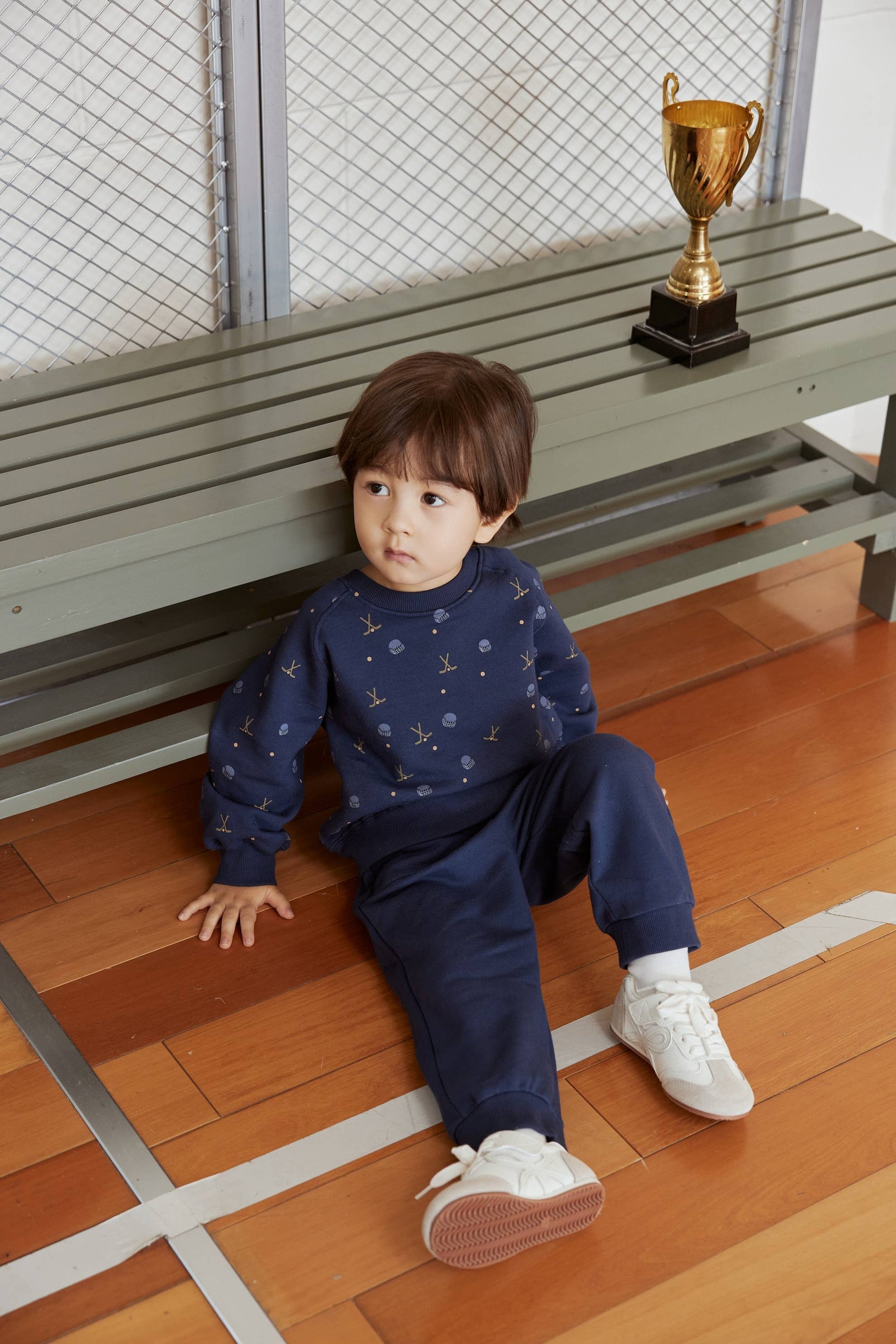 Child sitting on a wooden floor with a gold trophy in the background