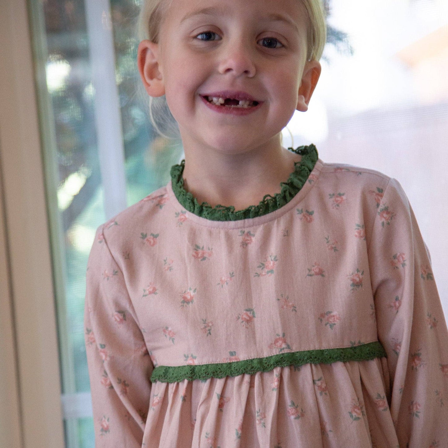 Young girl wearing a pink dress with green trim indoors
