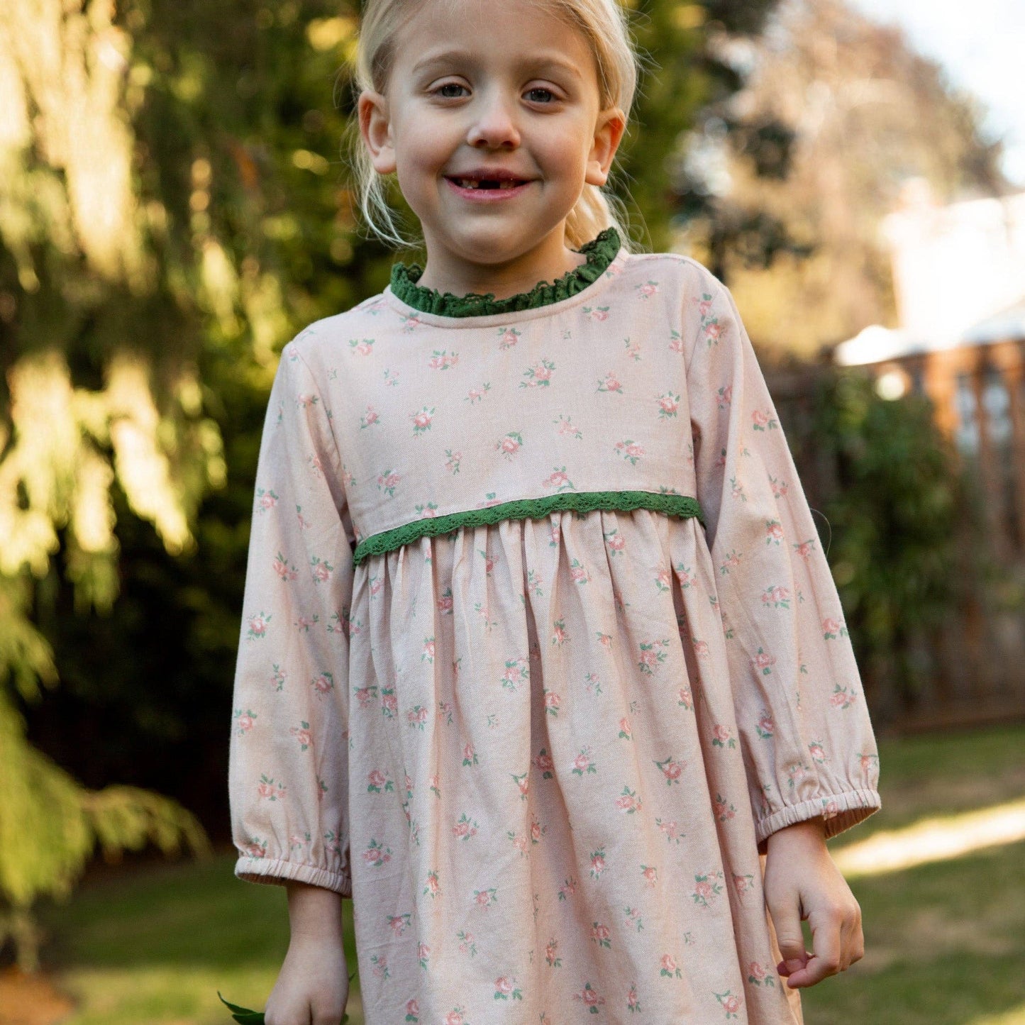 Young girl wearing a floral dress with green trim in an outdoor setting